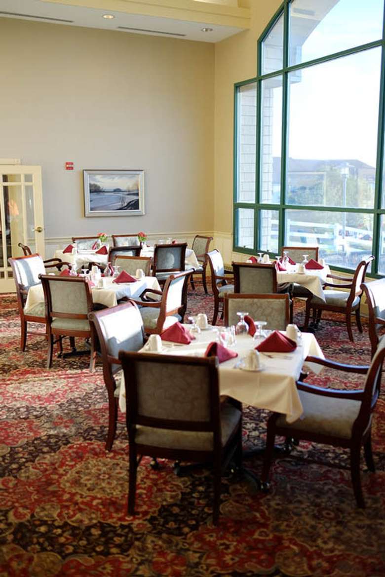 upscale dining room with white tablecloths, red napkins, a large window, and padded chairs with arm rests