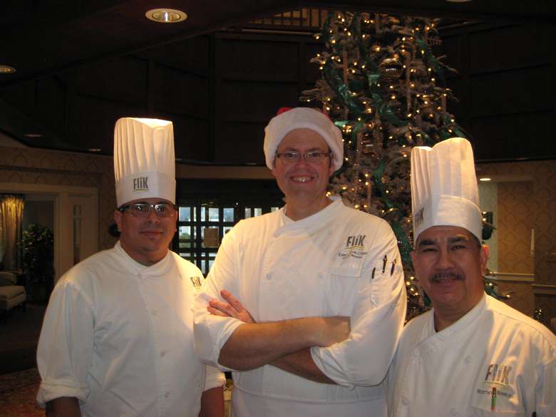 three chefs in white clothing, one of whom is wearing a santa hat