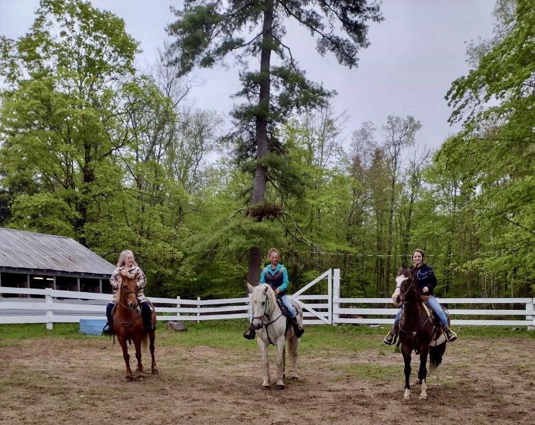 3 women on horses white fence and trees in background