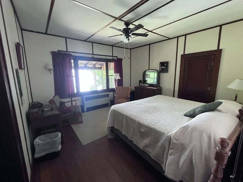 large bedroom with a bed, chairs, dresser, and ceiling fan