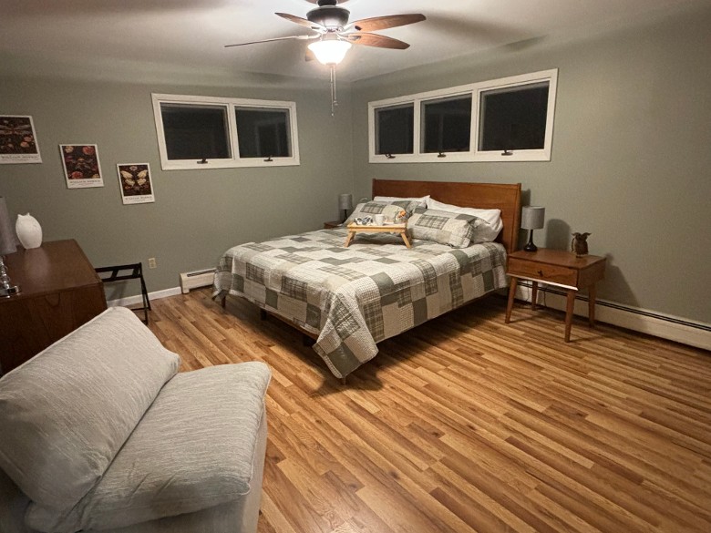 a bedroom with a bed, chairs, windows, ceiling fan, and wooden floor