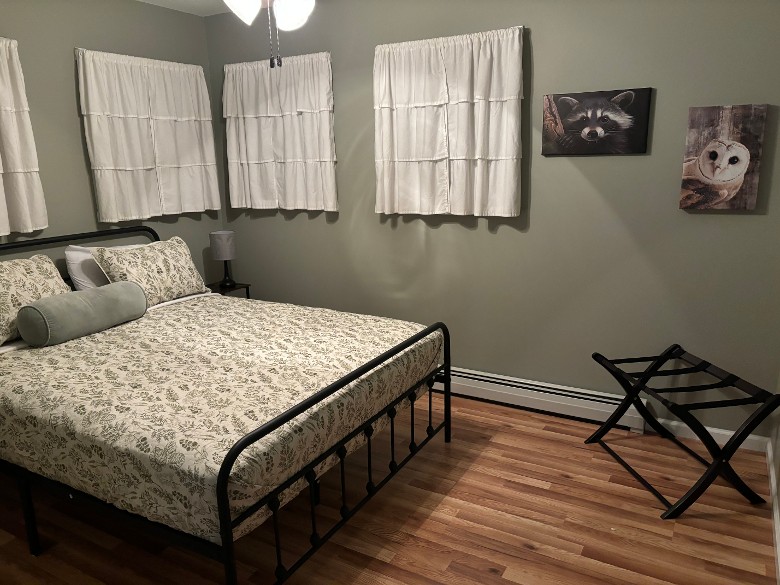 bedroom with a bed, wooden floor, and windows with white curtains in front of them