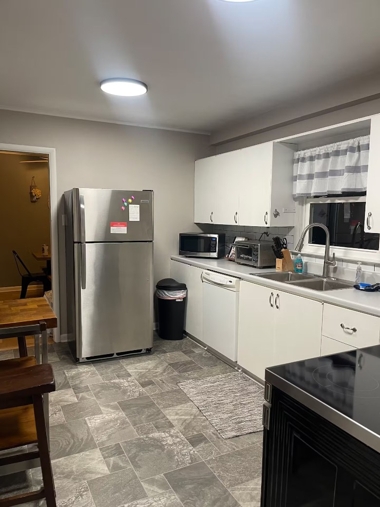 a kitchen with a fridge, white cabinets, and tile flooring