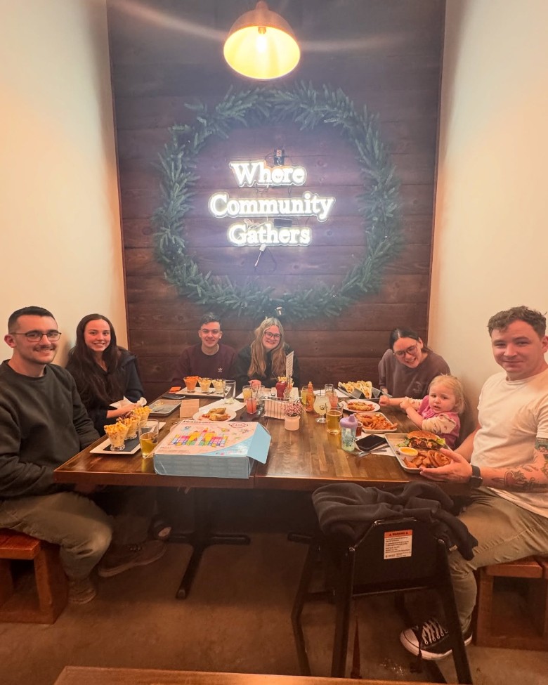 people seated inside at a table by a sign that says Where Community Gathers