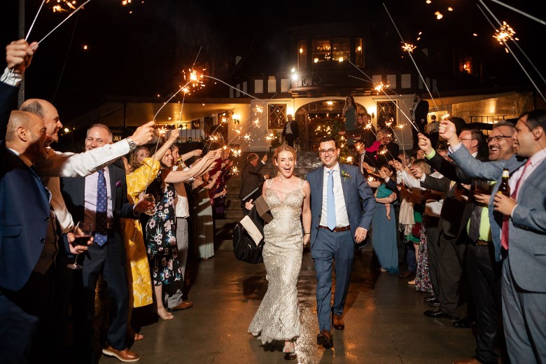 bride and groom walking down outdoor aisle while everyone holds sparklers at night