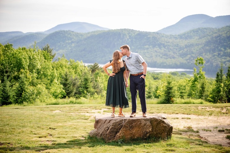 man and woman standing on rock and kissing with mountains in the back
