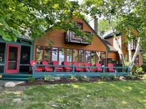 exterior of a large rustic house with a front deck and red Adirondack chairs