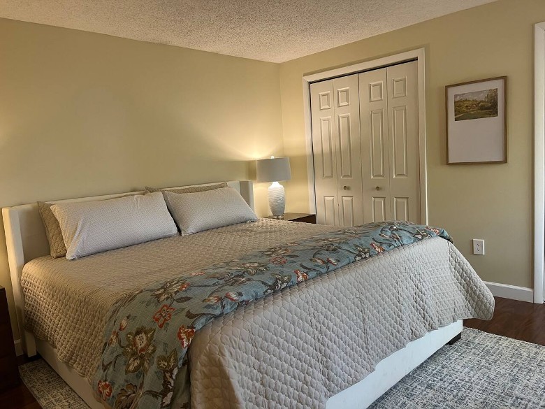 a house bedroom with a large bed, a quilt, a closet, and a lamp