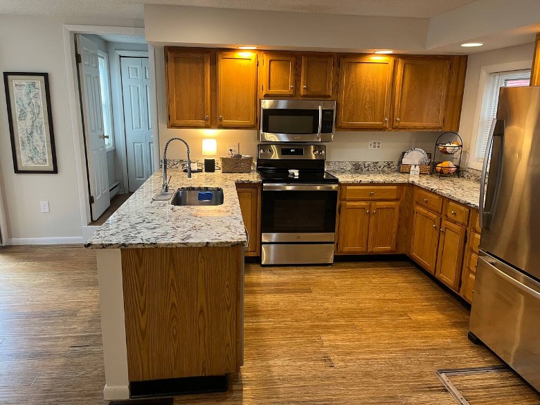 a kitchen with a granite countertop, appliances, and wooden floors and cabinets
