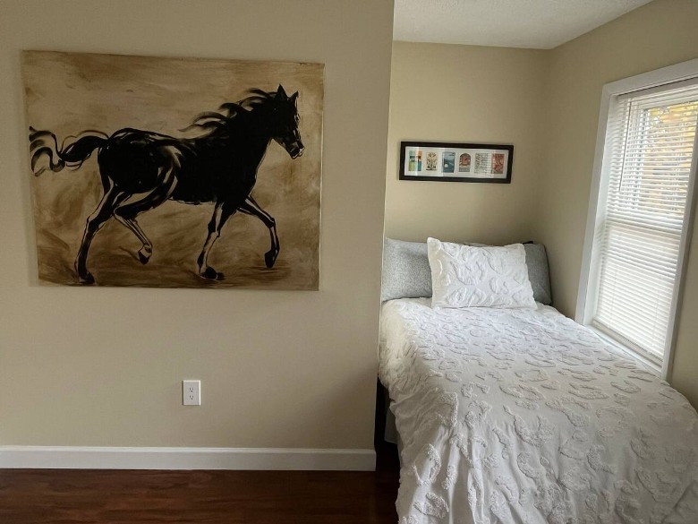 a house bedroom with a small bed, and a painting of a black horse on the wall