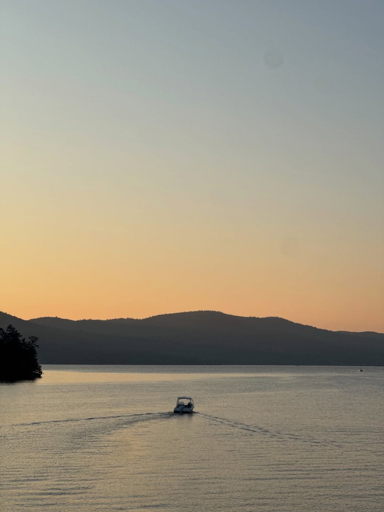 a boat heading out on a lake with sunset over the mountains