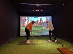 indoor golf instructor and woman preparing to swing