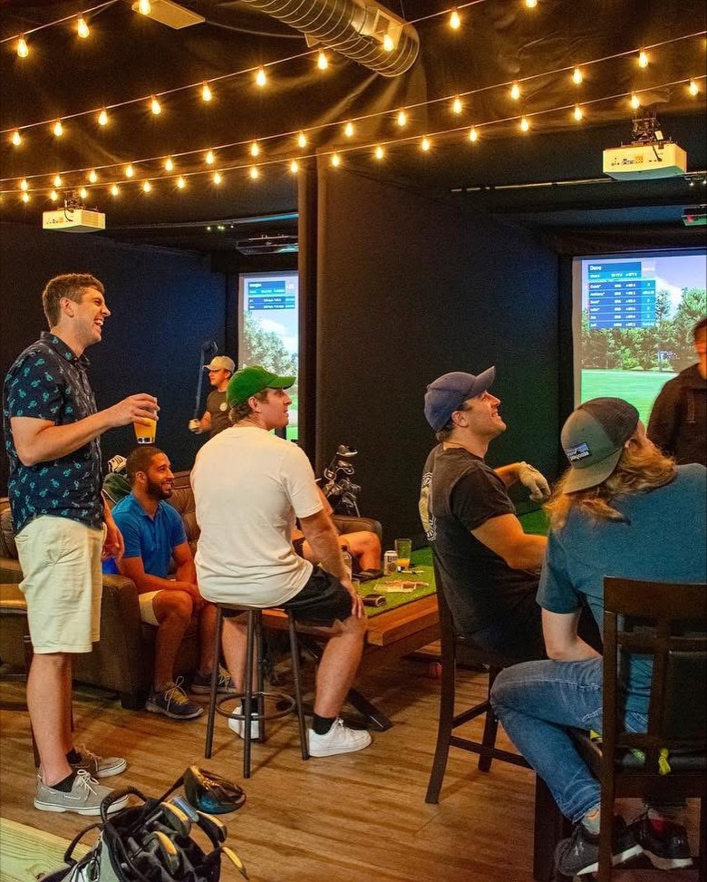 a group of people hanging out by an indoor golf simulator