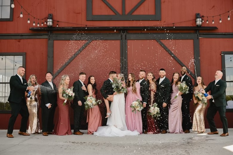 wedding party standing outside a red barn building and celebrating