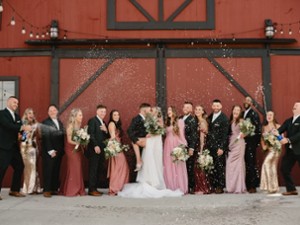wedding party standing outside a red barn building and celebrating