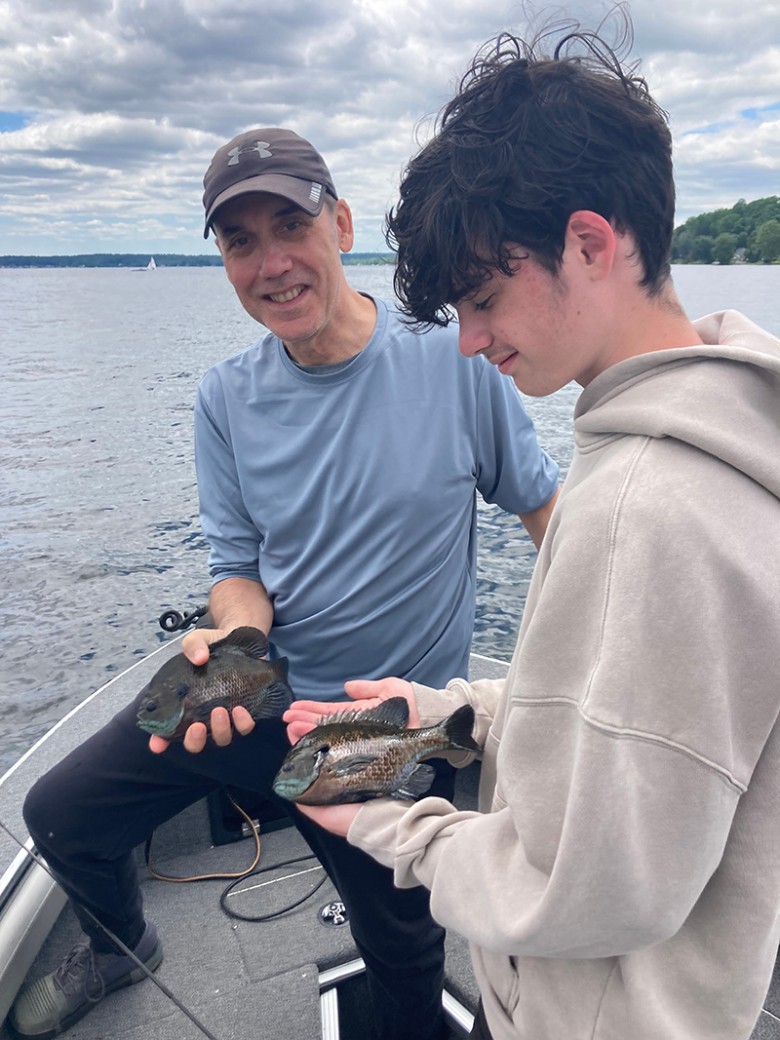 a man and teenage boy holding up small fish on a boat