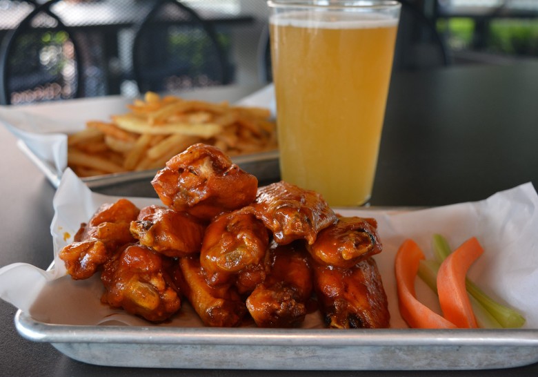 chicken wings with carrots and celery, next to a glass of beer and french fries on a patio table