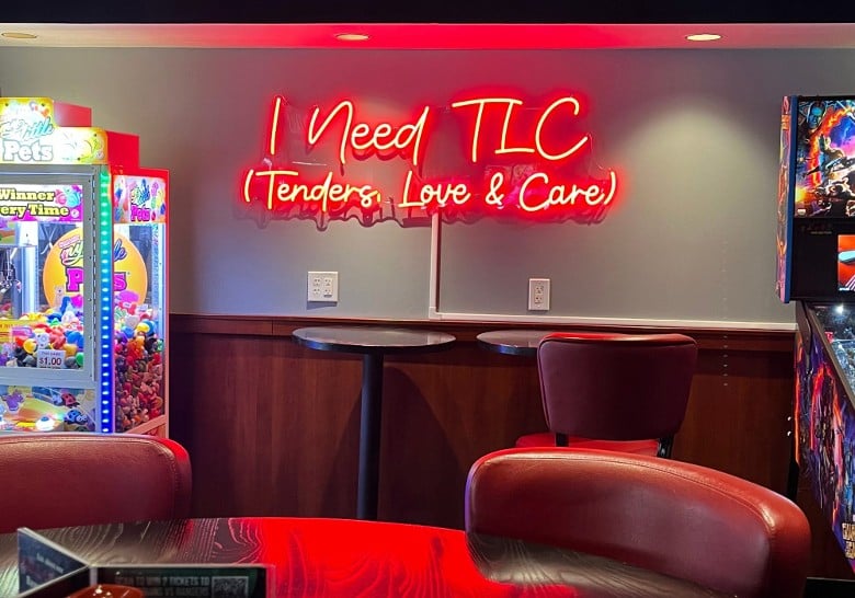 a neon sign on a restaurant wall that says I need TLC