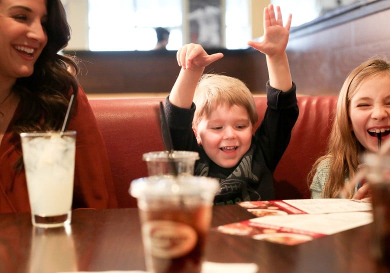 a woman, boy, and girl laughing at a restaurant table