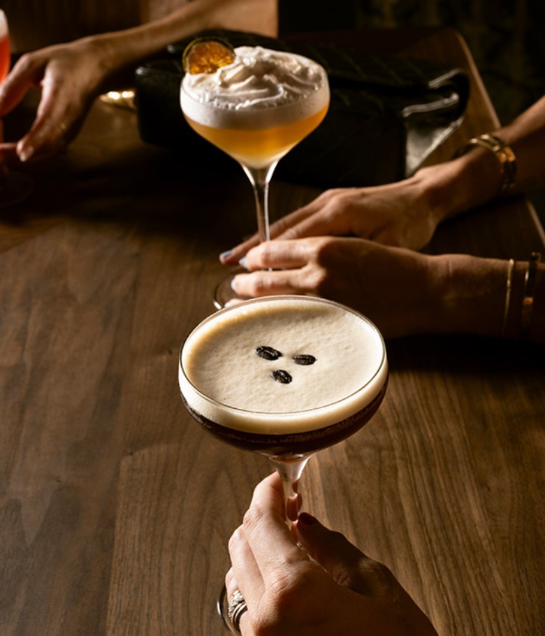 two cocktail glasses, one an espresso martini, and another with an orange slice on top