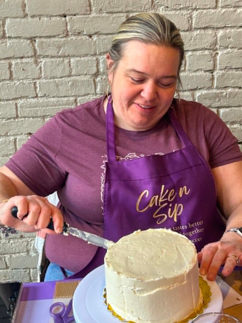 a woman putting buttercream on a cake