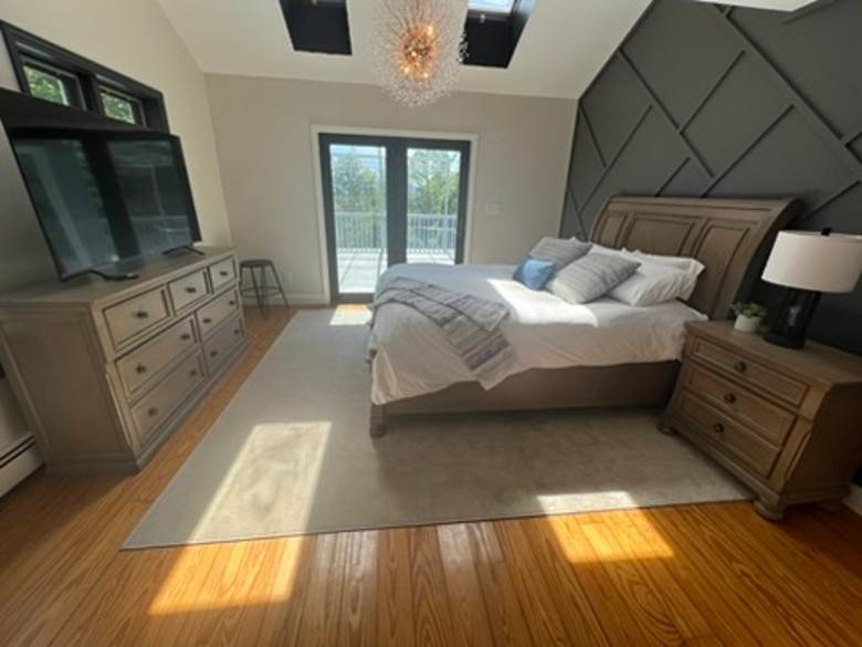 a large bedroom with a TV, bed, and sliding glass door leading to a deck