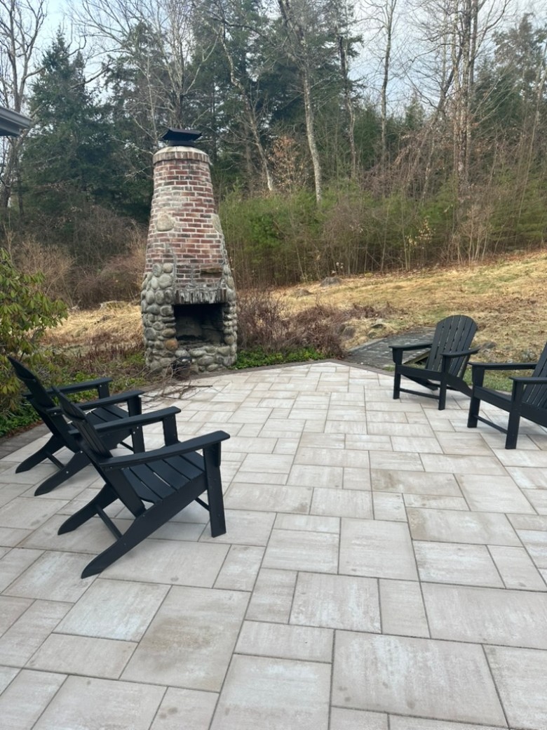 a stone patio with ADK chairs and an outdoor stone fireplace