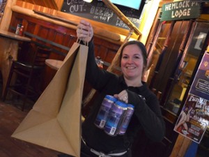 a woman holding up a four pack of beer and a brown paper bag with a handle