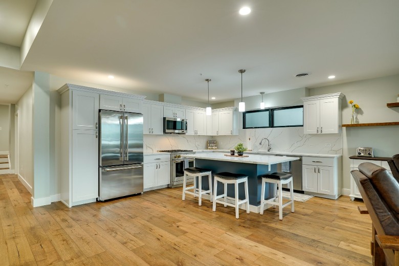 a modern kitchen with white cabinets, an oven, a fridge, a microwave, and an island with chairs