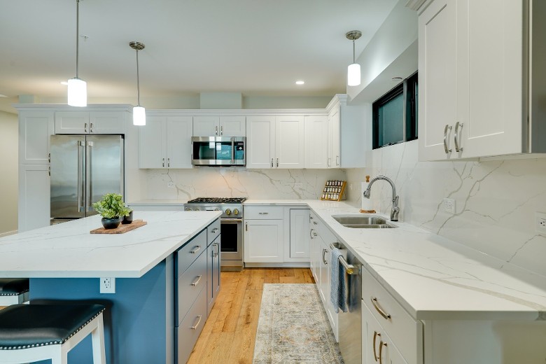a modern kitchen with white cabinets, an oven, a fridge, a microwave, and an island with chairs