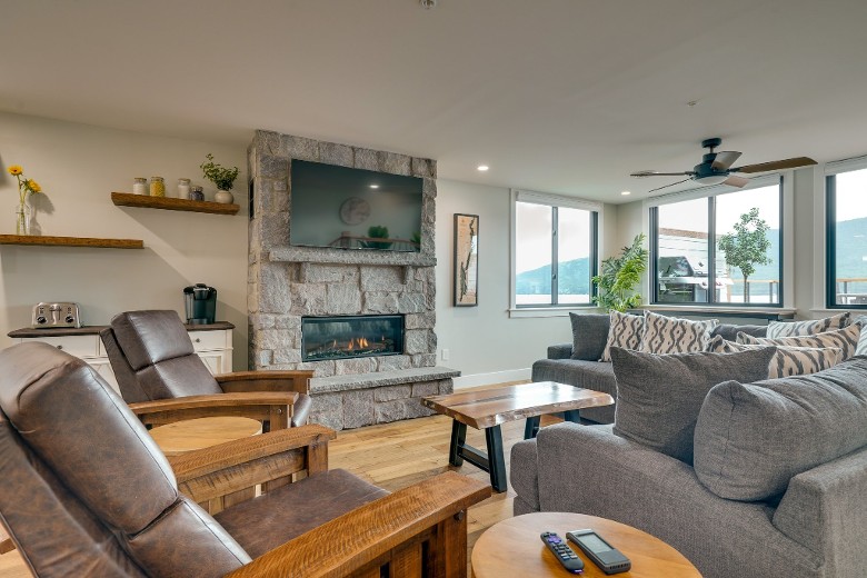 a living room with gray couches, chairs, a stone fireplace, and a TV above it on the wall