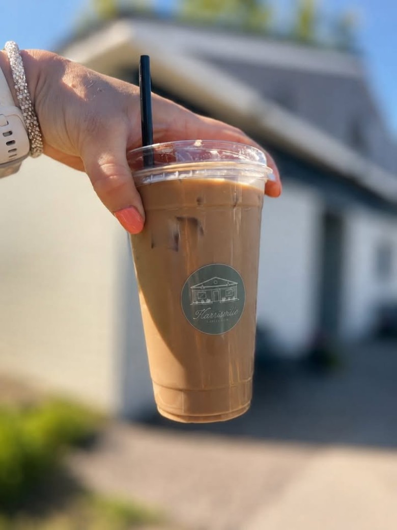 An iced coffee beverage from Harrisville Coffee Co., served in a branded cup. a person holding an iced coffee from the top