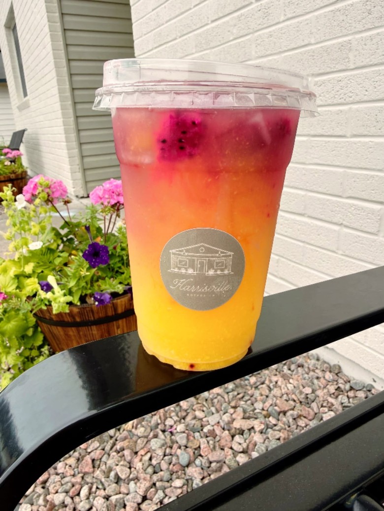 A specialty drink served outdoors near a flower display. a pink and yellow lemonade