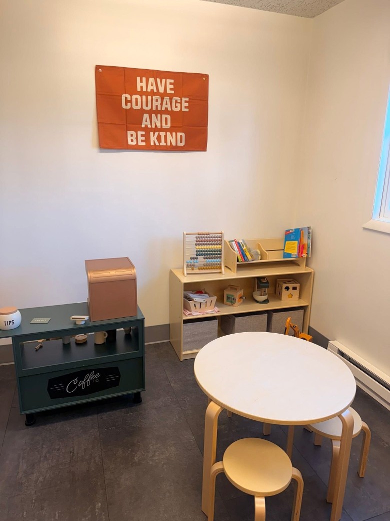 The café's family-friendly area, with books, activities, and seating for kids. a kids play area inside a coffee shop with a sign that reads have courage and be kind