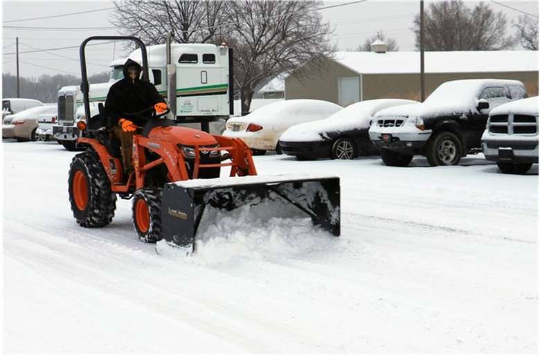 a person driving a small orange snow plow in winter