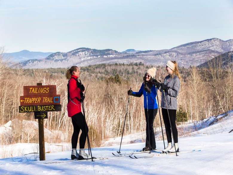 three cross country skiers on snowy slope near a trail sign