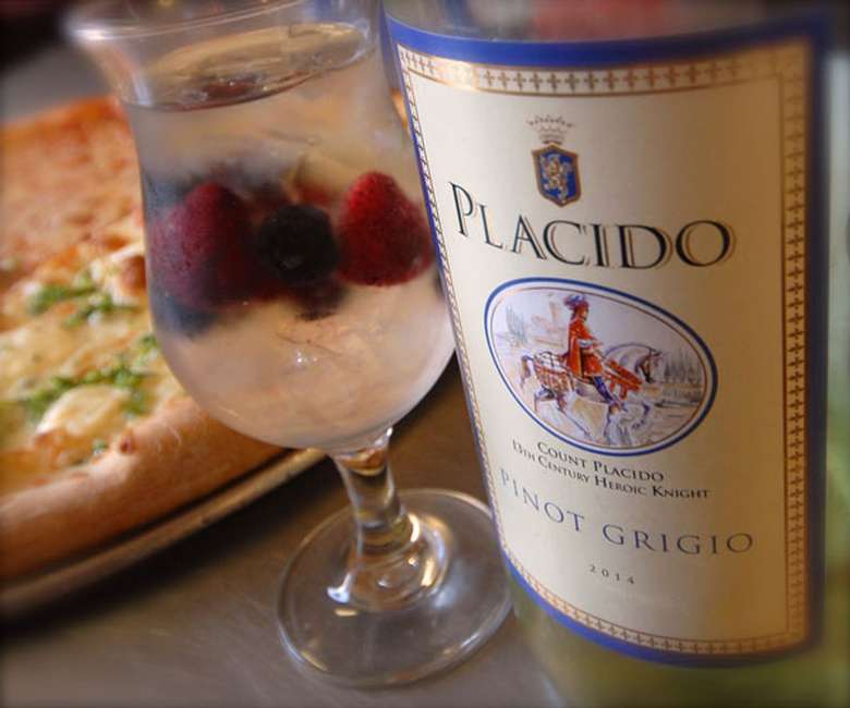 bottle of pino grigio in front of a mixed drink with a pizza in the background
