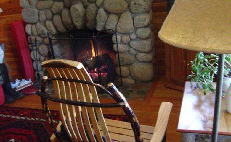 chair by stone fireplace that is lit with a fire