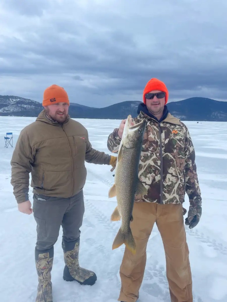 two men on frozen lake with one holding a fish