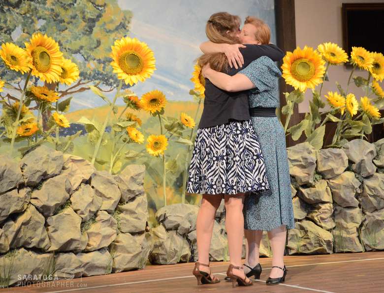 two actresses hugging on stage in front of a field of sunflowers