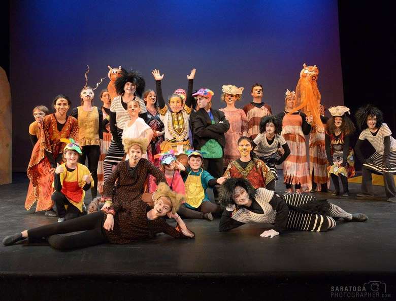 cast of a musical wearing tribal and animal style costumes posing on stage