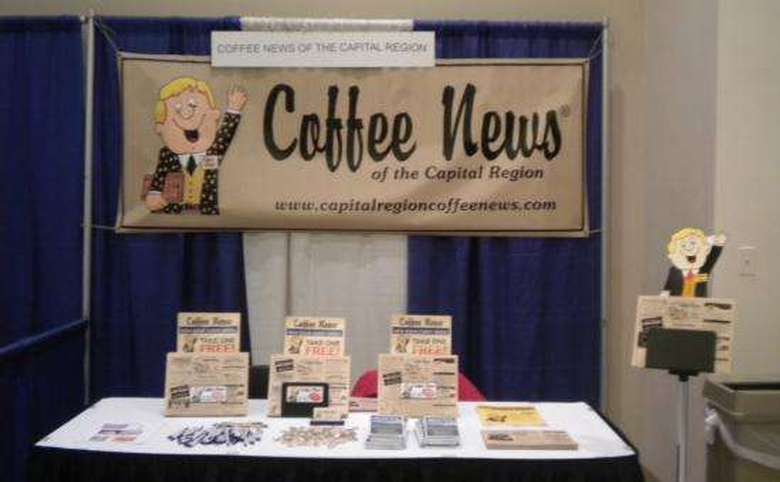 coffee news banner displayed at a trade show booth with brochures and promotional items