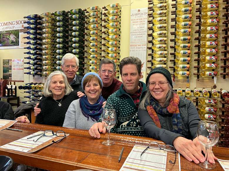 six people at a wine tasting bar with wine bottles in the back