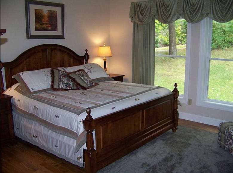 a bedroom with bed in a dark wood. There are large windows overlooking a green lawn