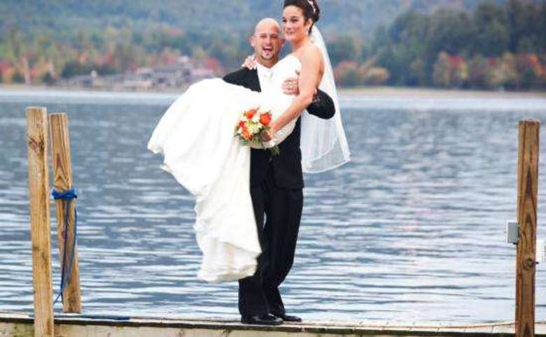 Man holding woman on dock in wedding attire