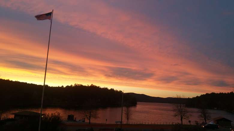 a sunset over a lake with a flagpole high in the sky