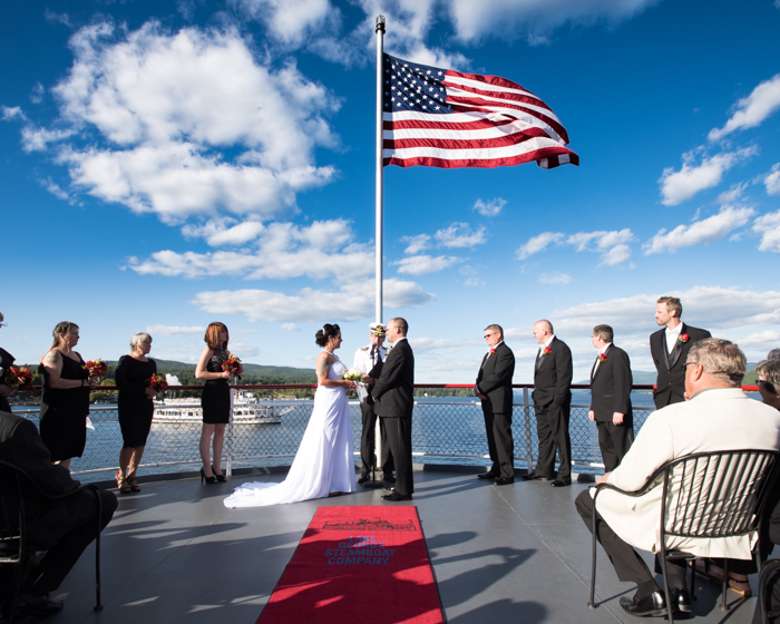 bride and groom getting married on the bow of a boat under a large american flag