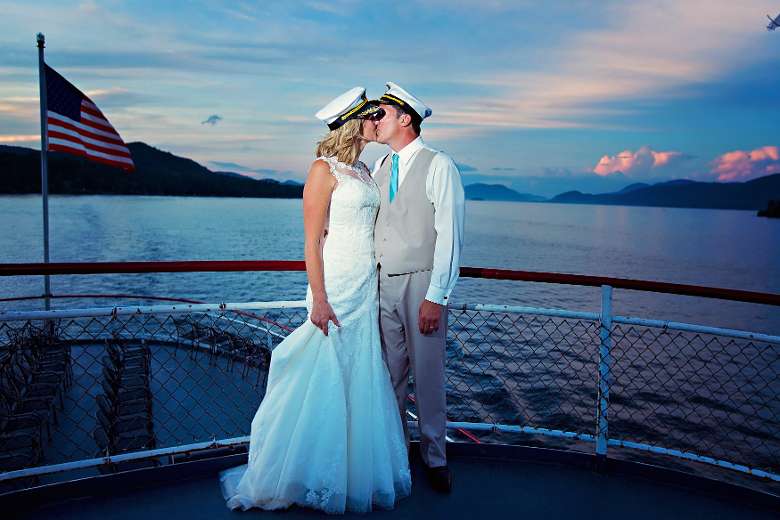 bride and groom wearing captain's hats and kissing on a large steamboat at sunset