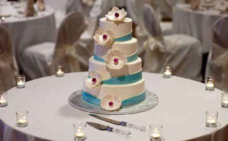 a four-tiered wedding cake, ivory with a teal stripe running up through it, surrounded by small candles