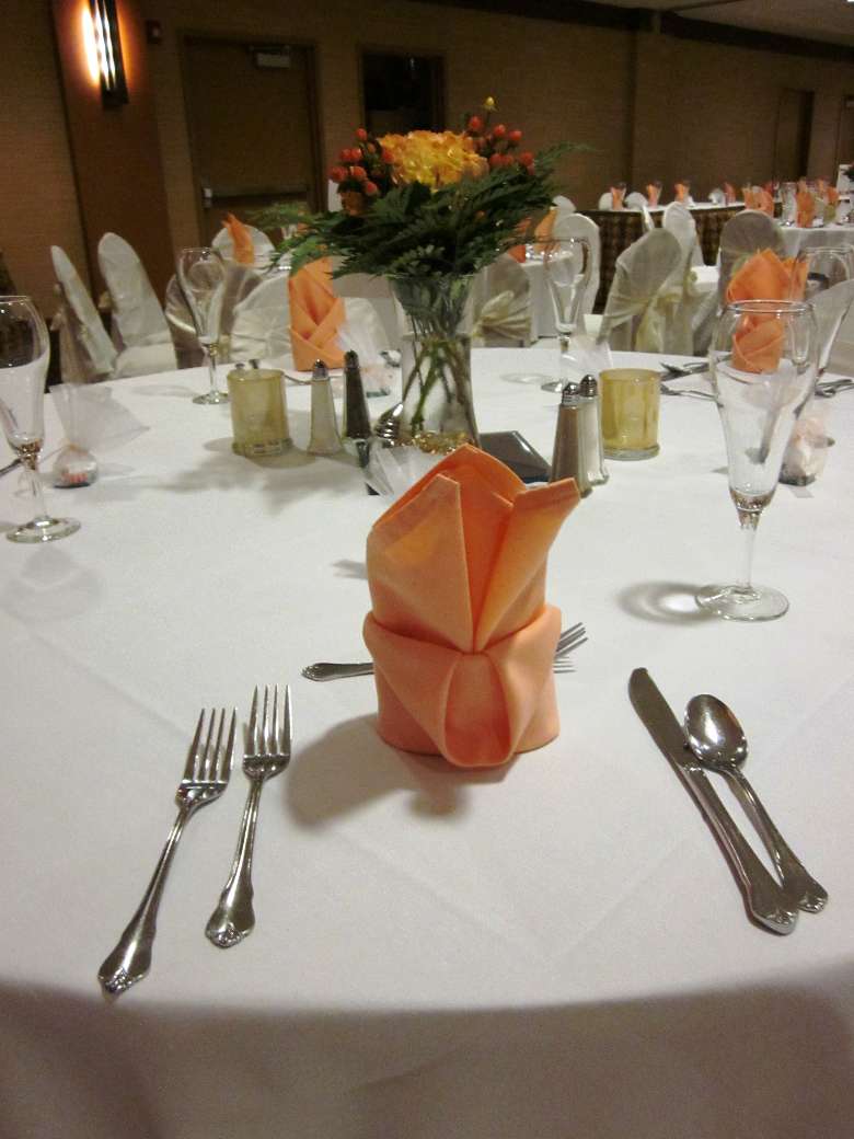 close up of a table setting at a wedding with a peach napkin folded where the plate would be and matching peach-colored flowers as a centerpiece